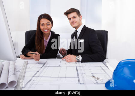 Junge Architekten arbeiten gemeinsam an Blaupause am Schreibtisch im Büro Stockfoto