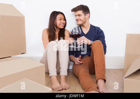 Junges Liebespaar Toasten Weingläser beim Sitzen am Boden im neuen Zuhause Stockfoto