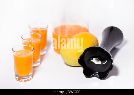 Tropische Früchte von Mango-Saft mit Schnapsgläsern und frische Mango-Frucht mit Stabmixer isoliert auf weißem Hintergrund schön Essen Fotografie Foto Stockfoto