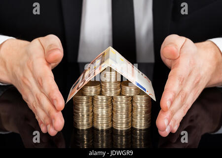 Mittelteil der junge Geschäftsmann schützen Haus gemacht Währung am Schreibtisch Stockfoto