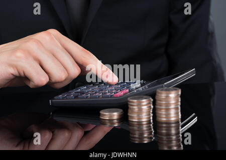 Zugeschnittenes Bild der Geschäftsmann mit Rechner von gestapelten Münzen auf Schreibtisch Stockfoto