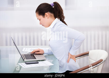 Junge Geschäftsfrau mit Rückenschmerzen sitzen vor Laptop Stockfoto