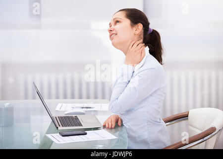 Junge Geschäftsfrau, die mit Schmerzen im Nacken am Arbeitsplatz Stockfoto
