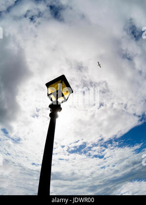 Vintage Straßenlaterne vor blauem Himmel mit weißen Wolken und Möwe in der Ferne Stockfoto