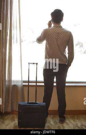 Rückansicht der Mann am Fenster telefonieren mit Trolley-Tasche Stockfoto