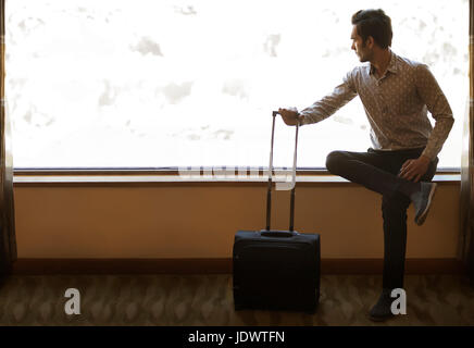 Junger Mann sitzt in der Nähe von Fenster halten Trolley-Tasche Stockfoto