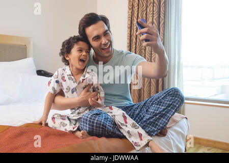 Vater und Sohn nehmen Selfie mit smart-Phone im Schlafzimmer Stockfoto
