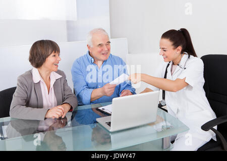 Lächelnd Ärztin geben Rezept Papier, älteres Paar am Schalter in Klinik Stockfoto