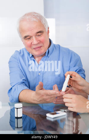 Ärztin mit Lancelot auf senior Mann am Schreibtisch in Klinik Stockfoto