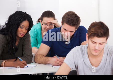 Studentinnen, die versuchen zu betrügen von männlichen Klassenkameraden während testen im Klassenzimmer Stockfoto