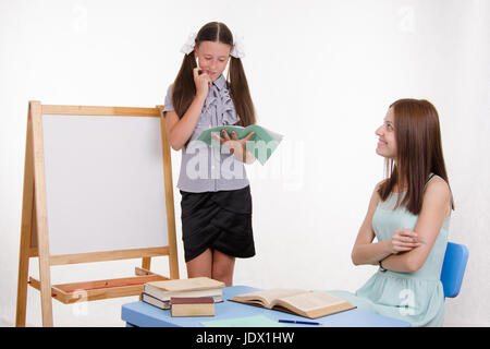 Schüler an der Tafel steht, der Lehrer sitzt an seinem Schreibtisch und hört auf den Schüler Stockfoto