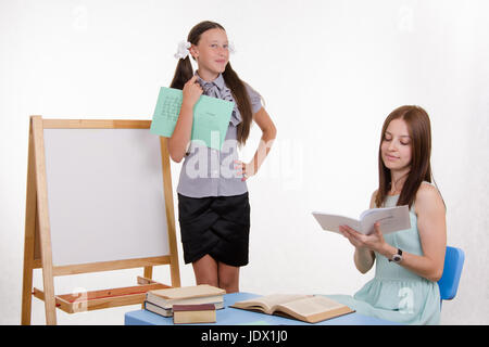 Schüler an der Tafel steht, der Lehrer sitzt an seinem Schreibtisch und hört auf den Schüler Stockfoto