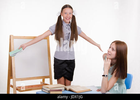 Schüler an der Tafel steht, der Lehrer sitzt an seinem Schreibtisch und hört auf den Schüler Stockfoto