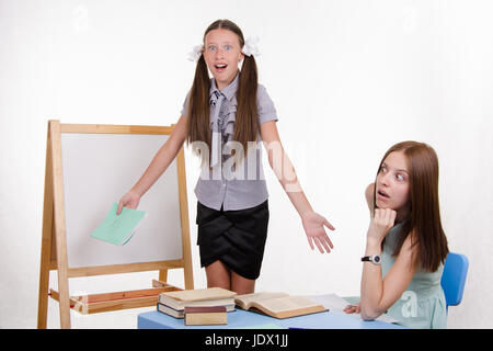 Schüler an der Tafel steht, der Lehrer sitzt an seinem Schreibtisch und hört auf den Schüler Stockfoto