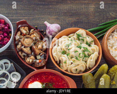 Russische Küche mit Textfreiraum. Sortiment-Gerichte der russischen Küche - Borschtsch, Pelmeni, Hering, marinierte Pilze, gesalzen, Gurken, Vinaigrette, sa Stockfoto