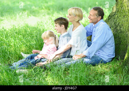 Vierköpfige Familie sitzen in Reihe unter Baum Stockfoto