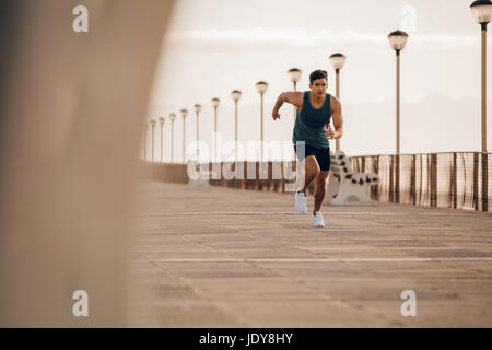 Voller Länge Schuss von Fit junge Mann läuft schnell auf der Promenade. Männliche Läufer sprinten Morgen. Stockfoto