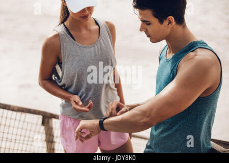 Junger Mann, der der Frau in der Pause eine Herzfrequenzanzeige zeigt. Fitnesspaare überprüfen ihre Trainingsleistung auf einer Smart Watch. Stockfoto