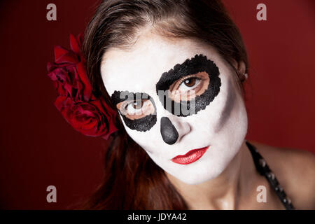 Frau mit Make-up von la Santa Muerte mit roten Rosen vor einem roten Hintergrund Stockfoto