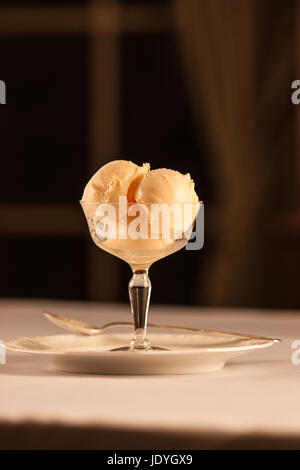 Schale von Orangen-Sorbet in eine Glasschüssel mit einem Löffel im Hintergrund. Stockfoto