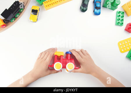 Ansicht von oben auf die Hände des Kindes spielen mit Spielzeugeisenbahn und vielen Spielsachen auf weißem Hintergrund. Stockfoto