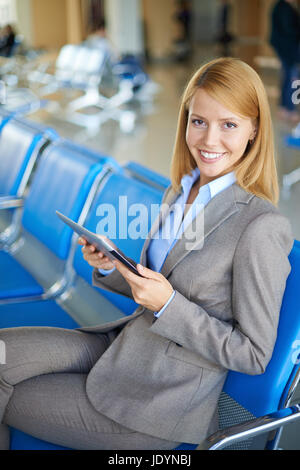Weibliche Angestellte mit Touchpad Blick in die Kamera während der Sitzung am Flughafen Stockfoto