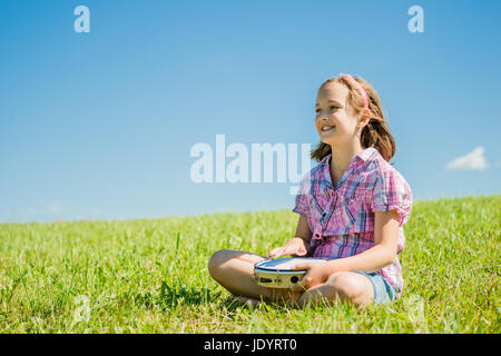 Cute Teen Mädchen spielen Tamburin sitzen auf dem Rasen in der Natur Stockfoto