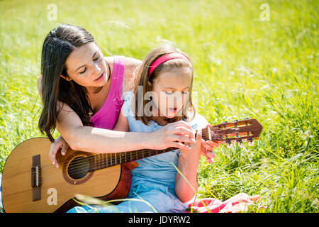 Mutter lehrt Plaing Gitarre ihr Kind - in der Natur an sonnigen Tag im freien Stockfoto