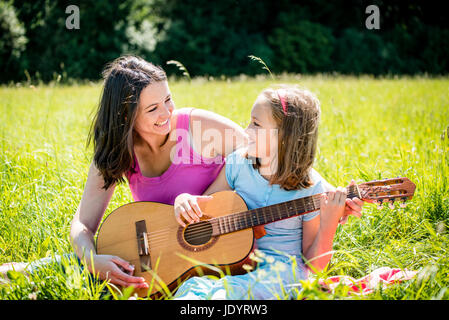 Mutter lehrt Plaing Gitarre ihr Kind - in der Natur an sonnigen Tag im freien Stockfoto