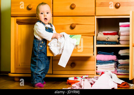 Baby wirft sich Kleider von Holzmöbeln zu Hause Stockfoto