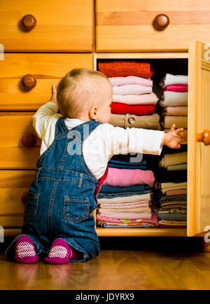 Baby wirft sich Kleider von Holzmöbeln zu Hause Stockfoto