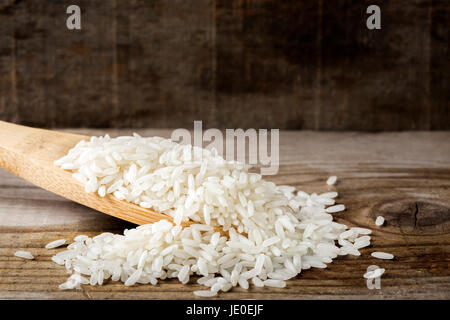 Holzlöffel, gefüllt mit Reis auf rustikalen hölzernen Hintergrund Stockfoto