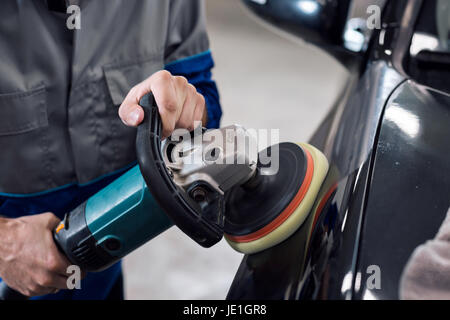 Nahaufnahme der Hände Arbeiter mit Schleifer, eine schwarze Karosserie in der Werkstatt zu polieren Stockfoto