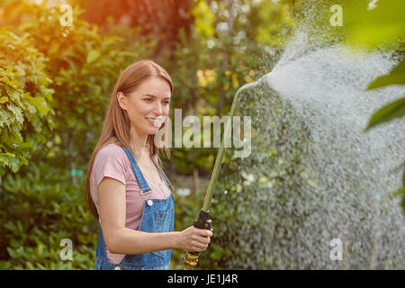 Gärtner Frau stehen und Spritzen Wasser auf Blumen mit Schlauch im Garten. Stockfoto