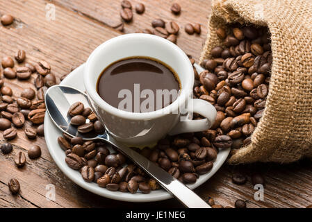 Tasse Kaffee mit Leinensack und Kaffeebohnen auf Holztisch. Stockfoto