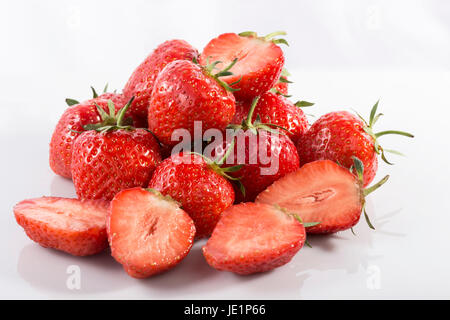 Viele Erdbeeren, ganze und halbierte, auf weißem Acryl mit einem weißen Hintergrund. Stockfoto