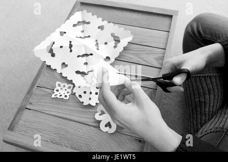 Frau mit einer Schere Papier gefaltetes in Schneeflocke Entwürfe - monochrome schneiden Verarbeitung Stockfoto