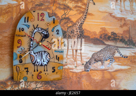 Farbenfrohe Wanduhr mit Giraffe an Wand mit Tapete Safari hautnah Stockfoto