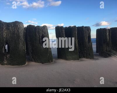 Bleibt ein Holzsteg am Strand in der Abenddämmerung, Coney Island, New York.  Verwitterte Holzmasten von einem Pier in den Sand in der Silhouette. Stockfoto