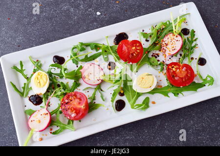 Frische Radieschen, Kirschtomaten, Wachtelei, Parmeggiano mit Balsamico-Glasur auf einem weißen Teller. Mediterranes Lebensgefühl. Gesunde Ernährung Stockfoto