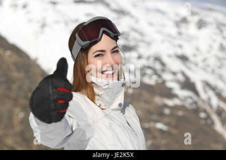 Positiven Skifahrer Frau gestikulieren Daumen im Winter mit verschneiten Bergen im Hintergrund Stockfoto