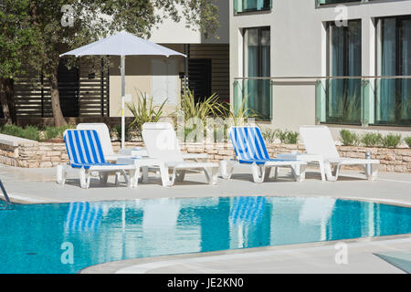 Sonnenliegen und Sonnenschirme am Pool an einem sonnigen Tag Stockfoto