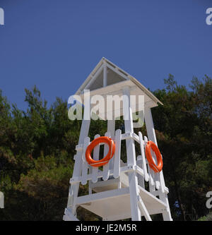 Rettungsschwimmer-Turm mit orange Rettungsring am Strand. Weiße Rettungsschwimmer-Turm mit Schwimmring an einem Sommerstrand in Chalkidiki, Griechenland. Stockfoto