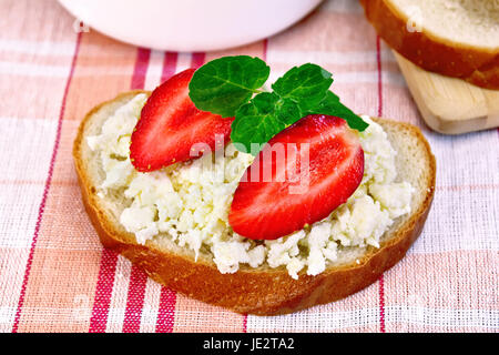 Ein Laib des Brotes mit Quarkcreme, Brot Minze und Erdbeeren, eine Schüssel mit Hüttenkäse, auf einem Brett auf einem Hintergrund von roten karierten Tischdecke Stockfoto