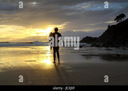 Ein Mann in seinen späten zwanziger Jahren zu Fuß den Strand zum Surfen. Stockfoto