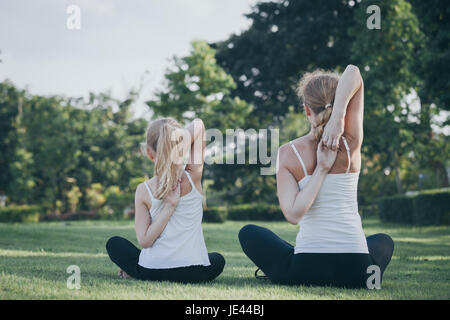 Mutter und Tochter, die Yoga-Übungen auf dem Rasen im Park an der Tageszeit zu tun. Leute, die Spaß im Freien. Konzept der freundliche Familie und der Sommer va Stockfoto