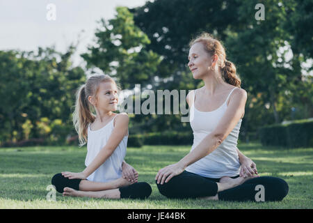 Mutter und Tochter, die Yoga-Übungen auf dem Rasen im Park an der Tageszeit zu tun. Leute, die Spaß im Freien. Konzept der freundliche Familie und der Sommer va Stockfoto