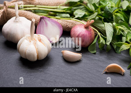 Knoblauch und Zwiebeln auf dem schwarzen Stein Tisch Stockfoto