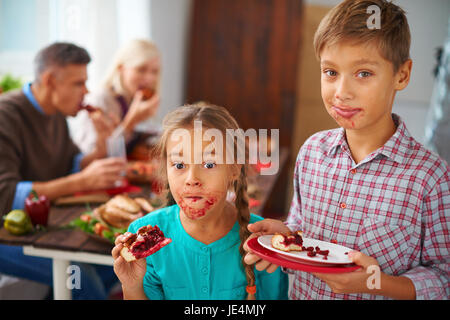 Porträt von lustigen Kinder Essen süßen Kuchen auf Hintergrund der Eltern Stockfoto