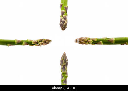 Vier grüne Spargelstangen ausgerichtet mit der horizontalen und vertikalen Achsen, fast gestalten ein Kreuz. Alle vier Spitzen sind bei der zentralen leere gerichtet. Gemüse, isoliert auf weiss. Stockfoto